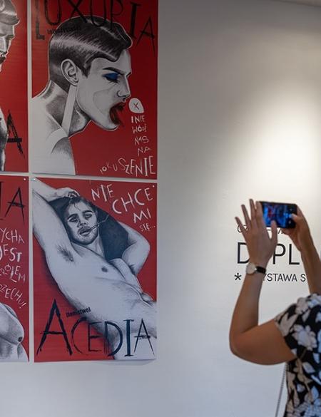 zdjęcie kobiety oglądającej prace w galerii, osoba robi zdjęcie smartfonem patrząc na grafiki