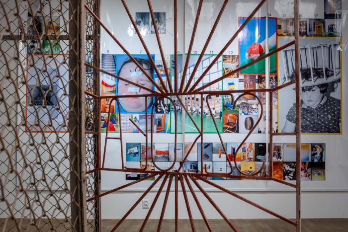 zdjęcie ukazujące fragment wystawy w gsw, brama z napisem szkoła, w tle układ licznych fotografii