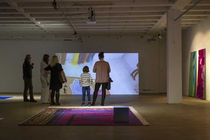 zdjęcie ukazuje ludzi w salach galerii oglądających film wideo na dużym ekranie