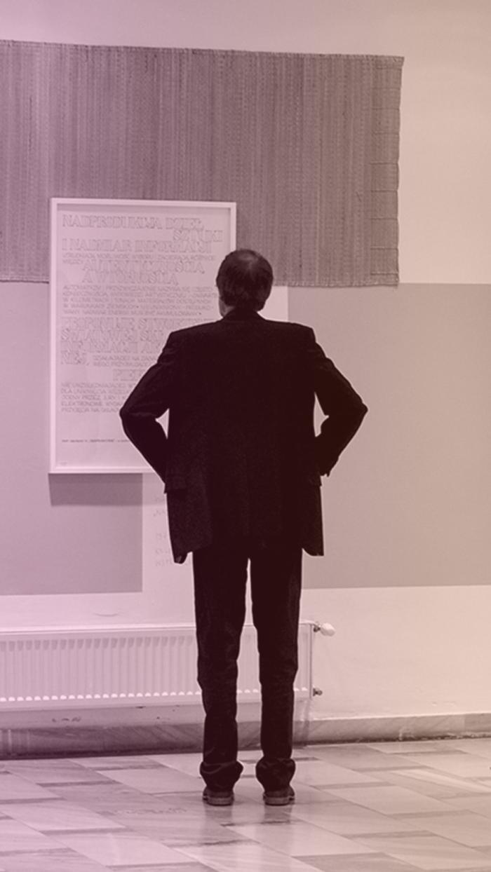 mężczyzna stoi przed pracami zawieszonymi na ścianie 